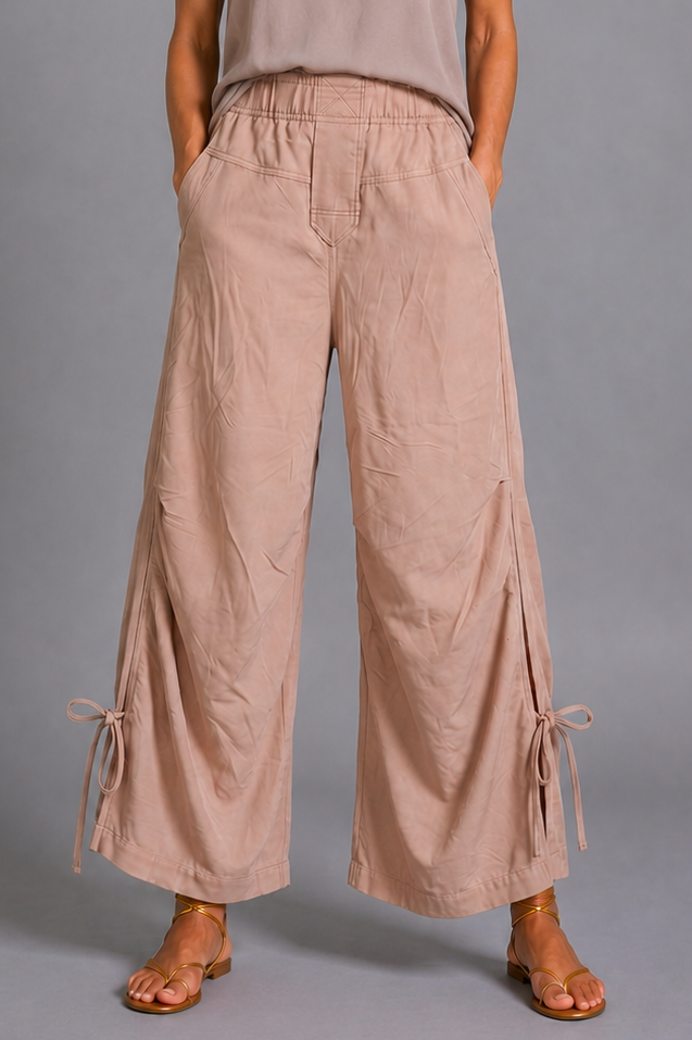 Woman wearing a beige tank top and wide-leg pants against a gray background